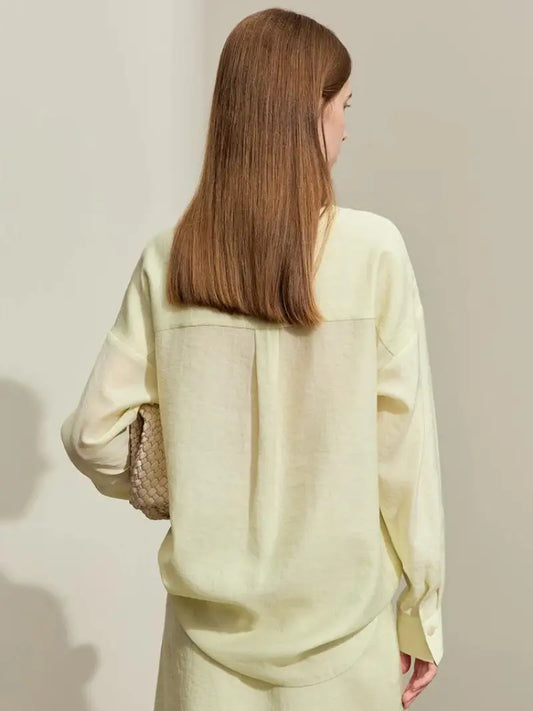 Une femme debout, dos à la caméra, vêtue d'un sweat-shirt oversize jaune clair et d'un pantalon assorti de la collection AMII Printemps 2024, tenant un sac tissé. Ses cheveux bruns raides
